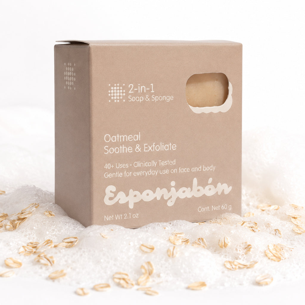 A square beige box of Esponjabén 2-in-1 Oatmeal Soothe & Exfoliate soap and sponge, styled on white foam with scattered oat flakes.