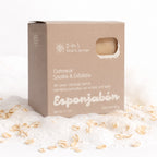 A square beige box of Esponjabén 2-in-1 Oatmeal Soothe & Exfoliate soap and sponge, styled on white foam with scattered oat flakes.