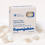 A white box of Esponjabón Mother of Pearl Brightening Effect soap and sponge, surrounded by iridescent mother-of-pearl stones and white powder on a clean white background.